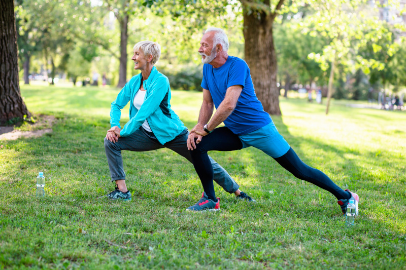 Ein älterer Mann und eine ältere Frau machen Sportübungen auf einer Wiese.